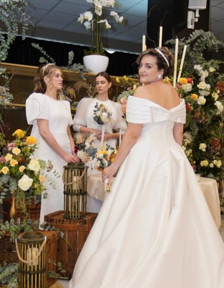Tres modelos con vestidos de novia ante una composición de flores y velas en Celebra Gandía 2025