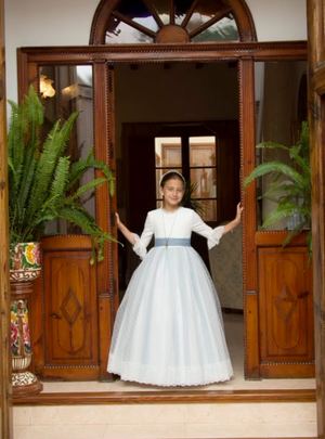 Niña con vestido de comunión de La Cuna Comuniones bajo el arco de una puerta de madera