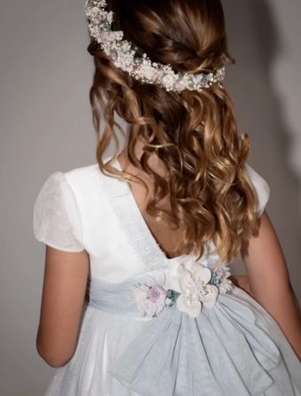 Vestido de comunión de La Cuna Comuniones visto de espaldas, con lazo azul, flores y corona de paniculata