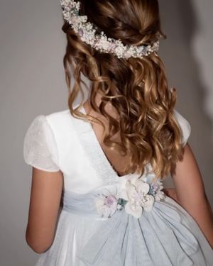 Vestido de comunión de La Cuna Comuniones visto de espaldas, con lazo azul, flores y corona de paniculata