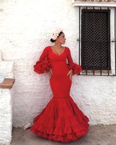Mujer con traje de flamenca rojo y tocado de flores de MonteColina Atelier junto a una pared encalada