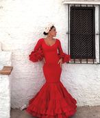 Mujer con traje de flamenca rojo y tocado de flores de MonteColina Atelier junto a una pared encalada